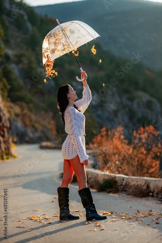 woman umbrella leaves , She holds him over her head, autumn leaves are falling out of him. Beautiful woman in a dress with an umbrella in the autumn park on the road in the mountains.