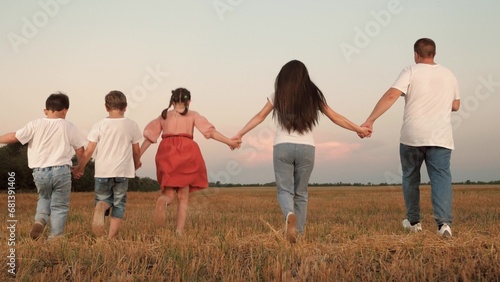 Strong family of parents and children run joining hands along field at sunset