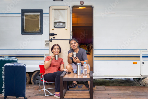 Senior asian couple joyful and relax sitting in front of caravan home on vacation.