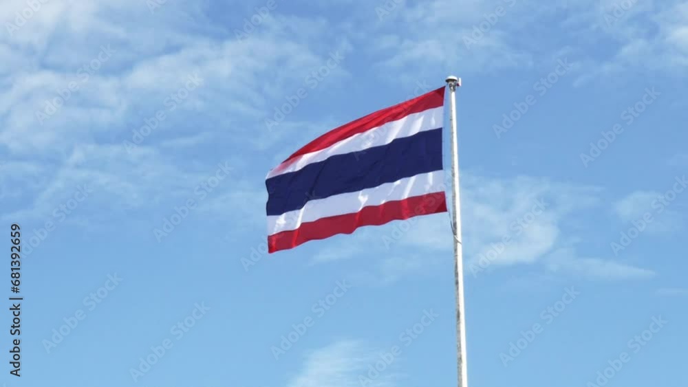 Thailand national flag hoisted on a white tall steel pole blown by the wind creating an animated wave on a backdrop of a clear blue sky and white clouds. Thailand national flag hoisted on a white tall steel pole blown by the wind creating an animated wave on a backdrop of a clear blue sky and white clouds.