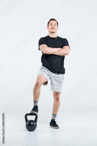 Isolated cutout full body studio shot of strong Asian male fitness athlete sportsman trainer in casual sport posing with kettlebell on white background.