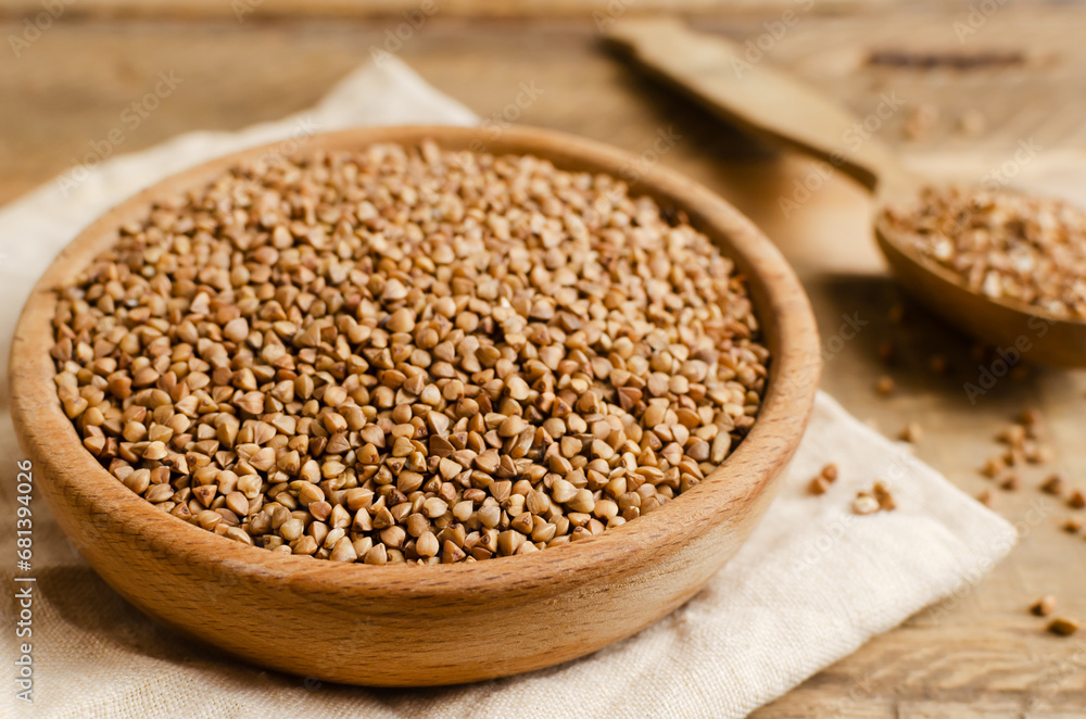 Organic buckwheat groats in a wooden bowl with spoon on a linen napkin on a wooden table. Rural style. Concept of healthy eating. Horizontal orientation. Selective focus Organic buckwheat groats in a wooden bowl with spoon on a linen napkin on a wooden table. Rural style. Concept of healthy eating. Horizontal orientation. Selective focus