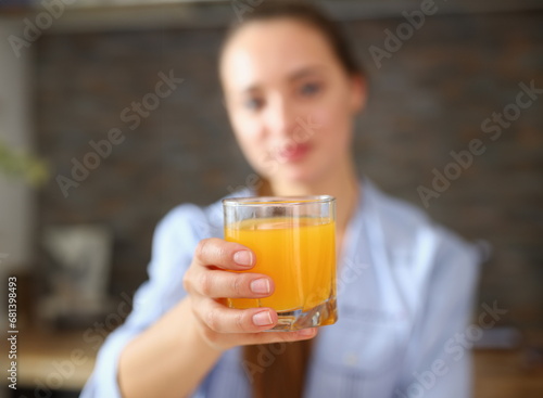Young beautiful attractive girl in pajamas in the kitchen drinking orange juice holding a glass in her hand © H_Ko