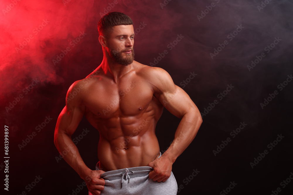 Young bodybuilder with muscular body in smoke on color background, space for text