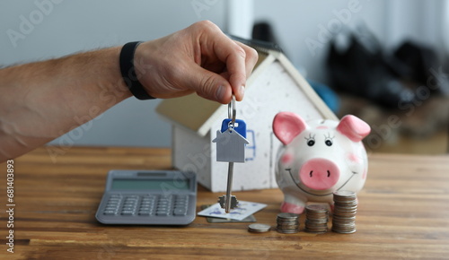 Wallpaper Mural Close-up of persons hand holding keys from new apartment. Cardboard model of house and piggy-bank with stacks of coins on wooden table. Property concept Torontodigital.ca