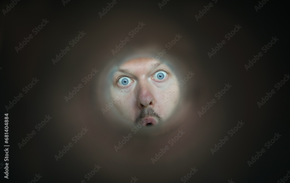 Focus on facial expression of person. Young guy with blue eyes looking through thin tube. Cheerful character with mustache and open mouth. Humorous person