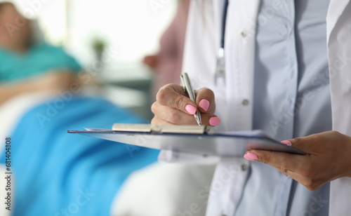 Focus on female hand holding paper folder and writing in important documents by pen. Female doctor asking well-being of patient. Healthcare and medicine concept
