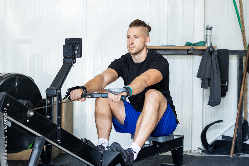 Fototapeta premium Fitness man on rowing machine doing exercises