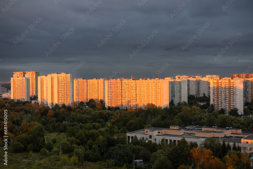 Tall multi-storey buildings in the rays of the setting sun. A beautiful residential area of the city at sunset against a cloudy sky. Multi-storey residential buildings in an urban area at sunset.