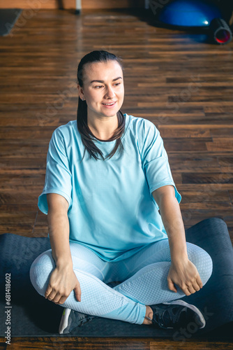 Young woman sitting on a mat in a fitness center, doing yoga and stretching. © puhimec