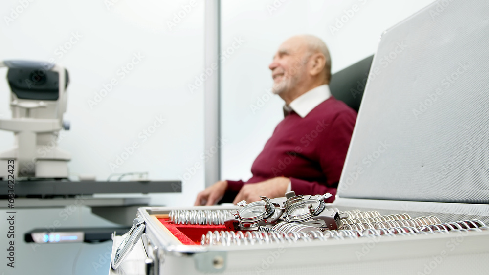Close-up of glasses for trial optometry in the hands of an ophthalmologist, with an elderly patient sitting in the background. An ophthalmologist checks a man's vision in the hospital. Close-up of glasses for trial optometry in the hands of an ophthalmologist, with an elderly patient sitting in the background. An ophthalmologist checks a man's vision in the hospital.