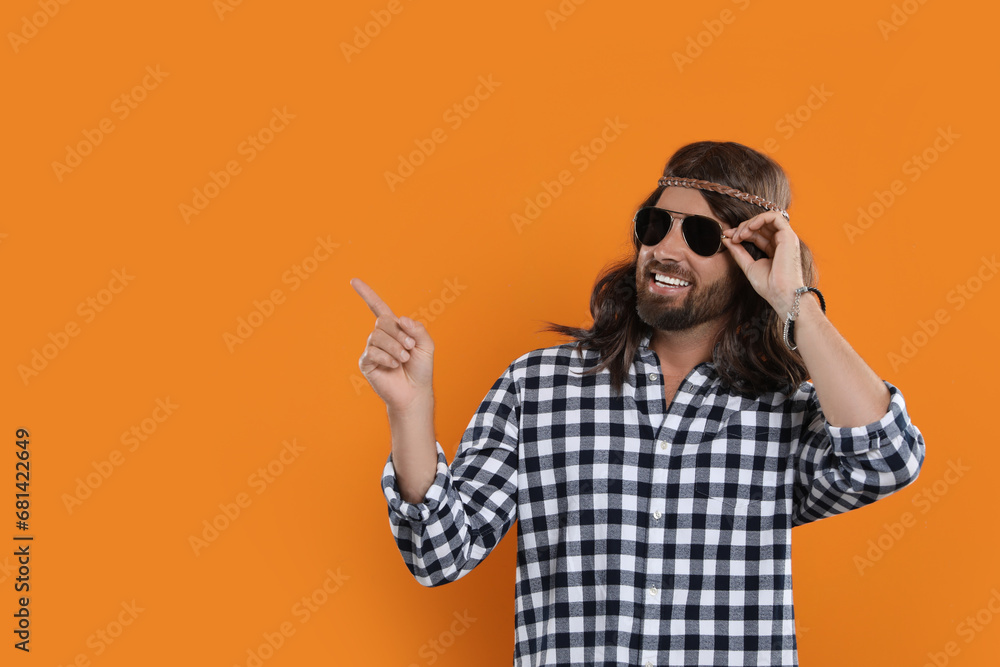 Hippie man in sunglasses pointing at something on orange background, space for text Hippie man in sunglasses pointing at something on orange background, space for text