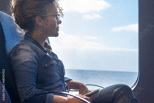 One woman traveling alone inside a ferry cruise with ocean and blue sky view. Concept of transport and business trip. Female people admire nature outdoor sitting on navy seat photo