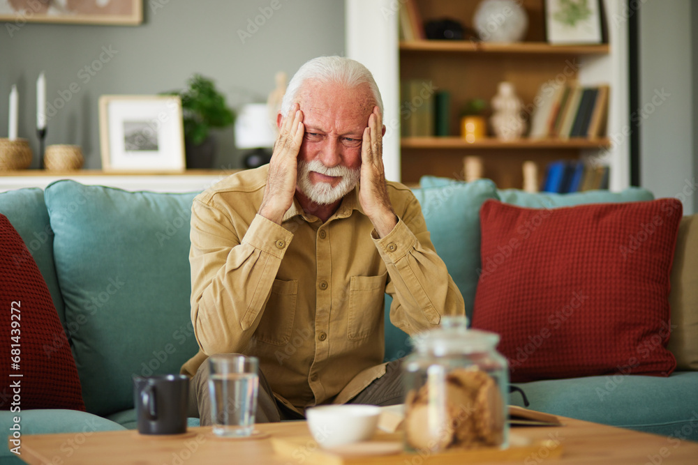 A senior man suffering from a migraine while sitting on the sofa in the living room A senior man suffering from a migraine while sitting on the sofa in the living room