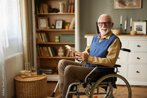 Elderly man in the wheelchair reading a book indoors