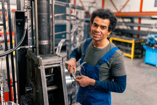 A mix race worker and workshop owner in overalls smiles and poses for an ad for his small business