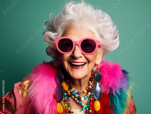 Funky grandmother laughing happily with fashionable clothes portrait  white hair and wearing trendy glasses a studio photo against neon background. Youthful grandmother with extravagant style