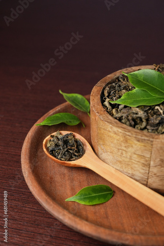 Dry tea with green leaves in wooden bowl and spoon on dark wooden table. Medicinal herbal collection. Banner. Side view.