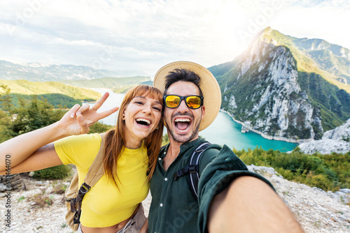 Happy couple taking selfie pic with smart mobile phone on top of the mountain - Young hikers climbing the cliff - Sport, technology and travel life style concept photo