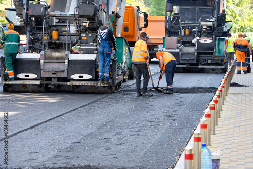 A team of road workers with asphalt pavers lay down fresh asphalt on a city street on a summer day. photo