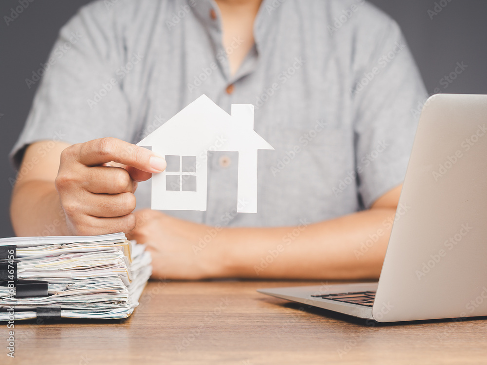 Fototapeta premium Businessman holding a mini paper house symbol while sitting at the desk