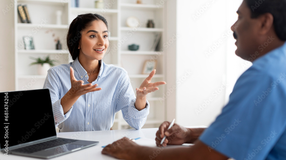 Young Indian Female Patient Talking To Male Doctor During Meeting In Clinic Young Indian Female Patient Talking To Male Doctor During Meeting In Clinic