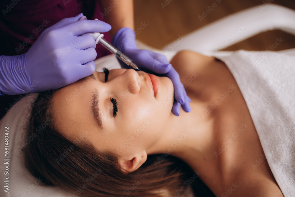 Fototapeta premium A woman with beautiful clear skin. A cosmetologist makes injections to increase the lips and anti-wrinkles of a beautiful woman. Women's cosmetology in a beauty salon.