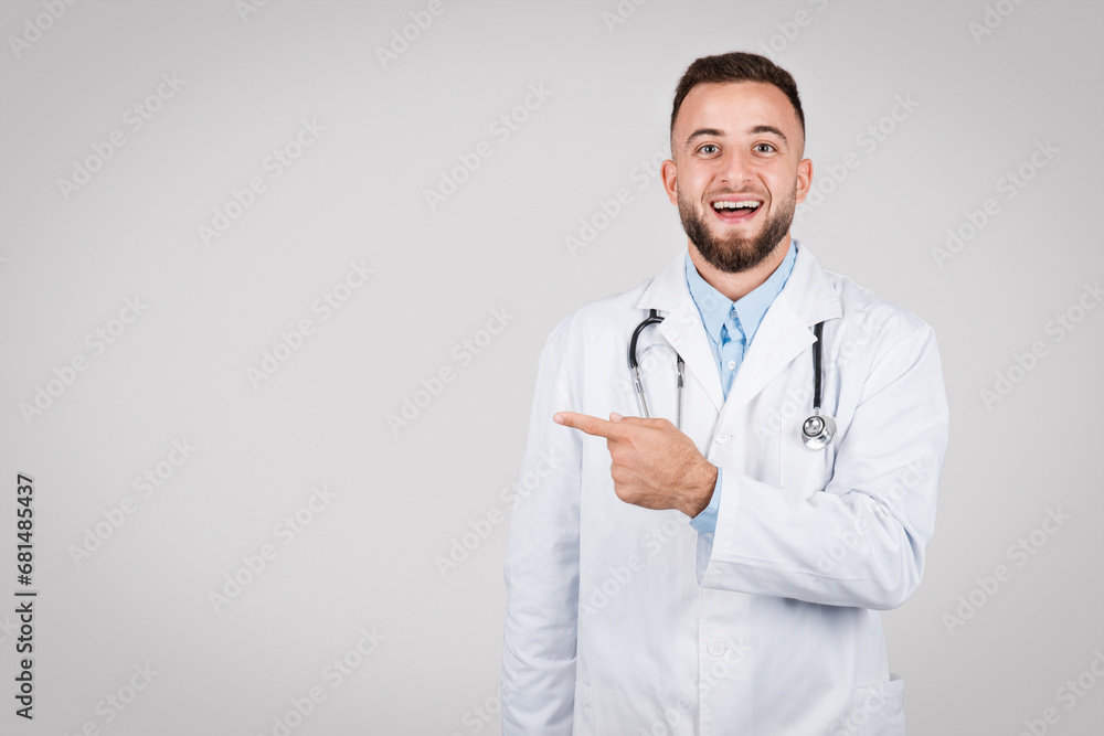 Joyful young male doctor pointing to the side at free space Joyful young male doctor pointing to the side at free space
