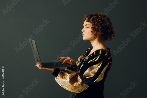 Young adult woman dressed in a medieval dress working on a laptop. Profile portrait