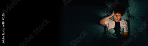 Young man suffering from insomnia uses a smartphone at night, addiction and stress concept photo
