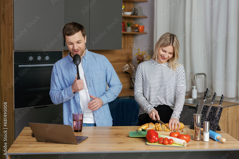 Home concert. Playful spouses having fun in kitchen, singing and dancing. Cheerful couple using kitchen utensils as microphones, fooling while cooking lunch at home. Home concert. Playful spouses having fun in kitchen, singing and dancing. Cheerful couple using kitchen utensils as microphones, fooling while cooking lunch at home.