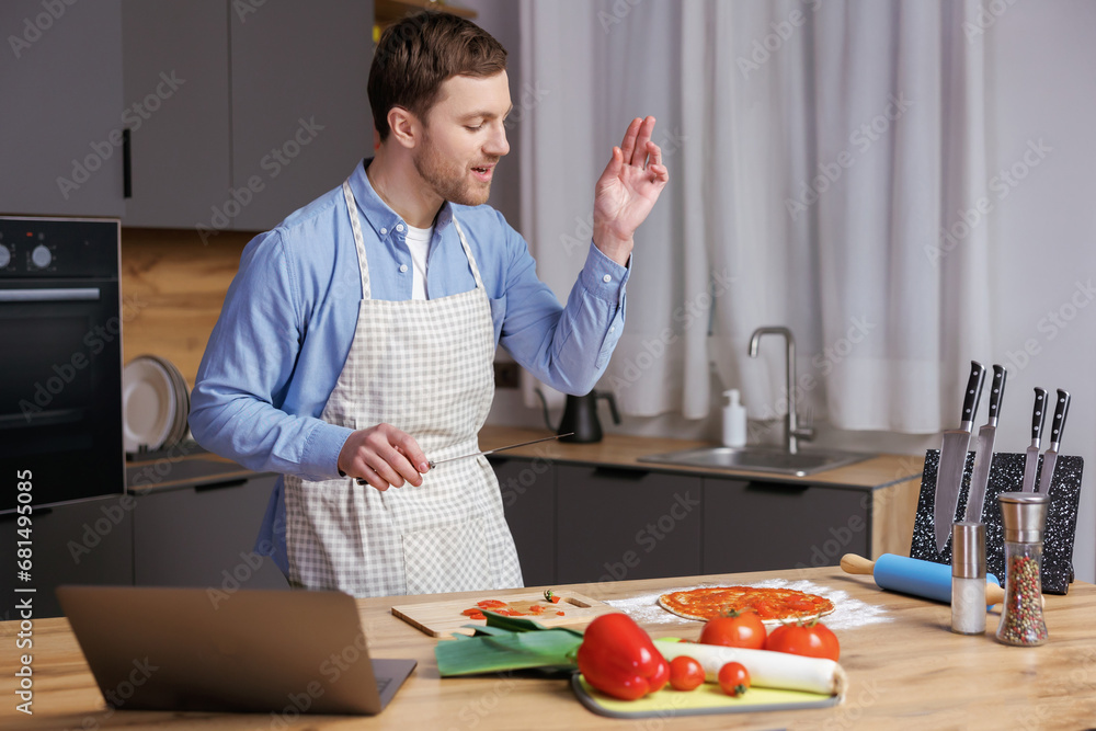 Young handsome man is preparing pizza and salad in the kitchen. The man enjoys the process of cooking. Young handsome man is preparing pizza and salad in the kitchen. The man enjoys the process of cooking.