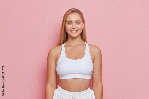 Portrait photo of happy sportswoman dressed in white top posing in pink studio smiling, beauty concept, copy space