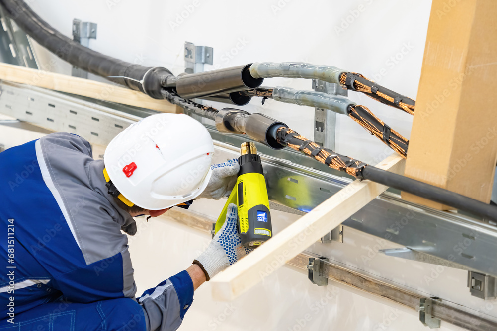 Man is doing electrical work. High voltage cable insulation. Guy uses construction dryer to heat