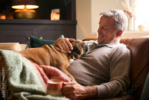 Mature Man At Home In Jumper With Hot Drink Of Tea Or Coffee In Cup Stroking Pet French Bulldog
