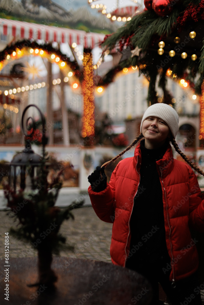 The young woman in white cap and red jacket portraits, playing with her pigtails on the Christmas market