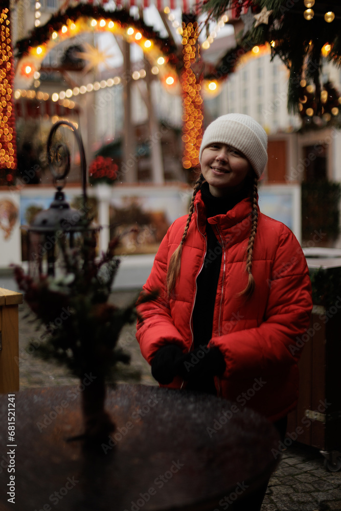 The young woman in white cap and red jacket portraits, playing with her pigtails on the Christmas market