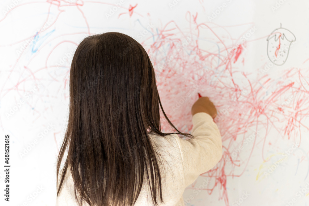 壁のホワイトボードに落書きする女の子の後ろ姿(3歳、日本人)