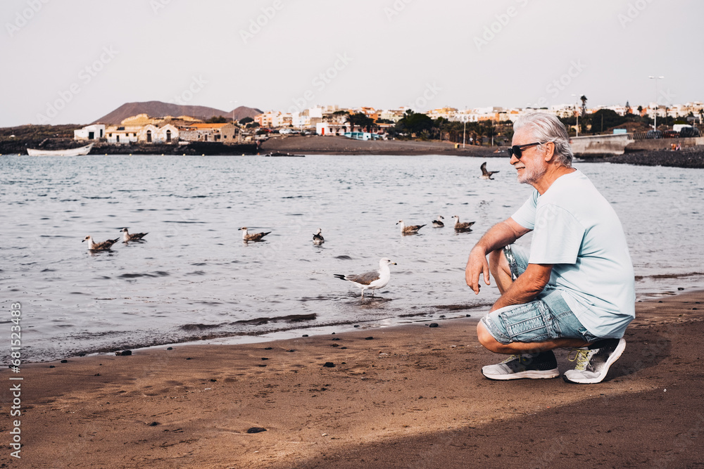 Carefree senior bearded man at sunrise on the sea shore looking at sea birds enjoying freedom and nature, vacation or retirement concept Carefree senior bearded man at sunrise on the sea shore looking at sea birds enjoying freedom and nature, vacation or retirement concept