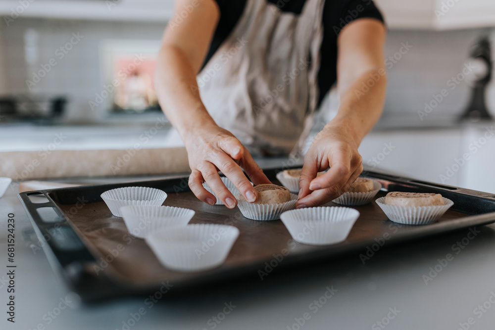 View of woman's hands putting raw cinnamon bun into cupcake case View of woman's hands putting raw cinnamon bun into cupcake case