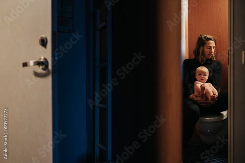 Mother sitting on toilet and holding naked baby photo