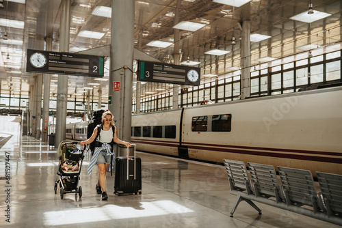 Mother walking with baby stroller and wheeled luggage at train station photo