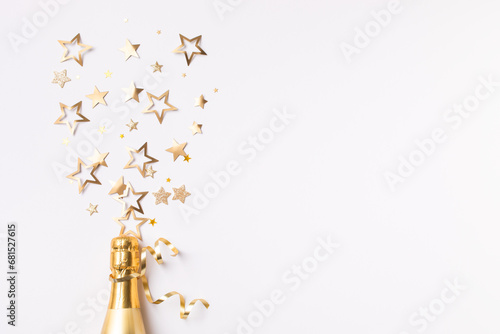 Champagne bottle with confetti stars and party streamers on white festive background. Christmas, birthday or wedding concept. Flat lay.