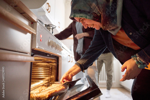 Woman taking food for eid al-fitr out of oven photo