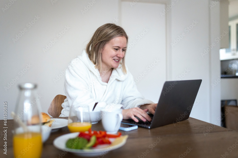 Smiling blond woman using laptop at dining table Smiling blond woman using laptop at dining table