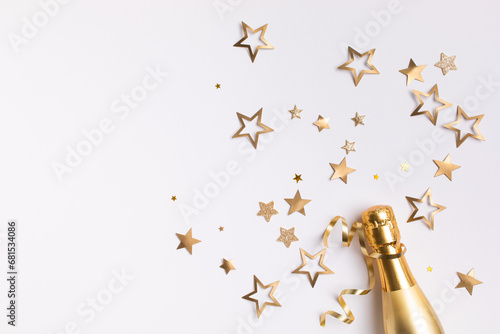 Champagne bottle with confetti stars and party streamers on white festive background. Christmas, birthday or wedding concept. Flat lay.