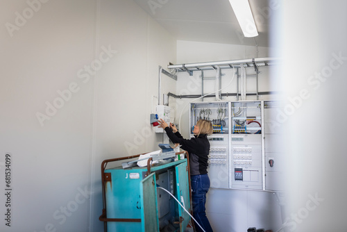 Female electrician installing fuse box while standing in meter room at industry photo