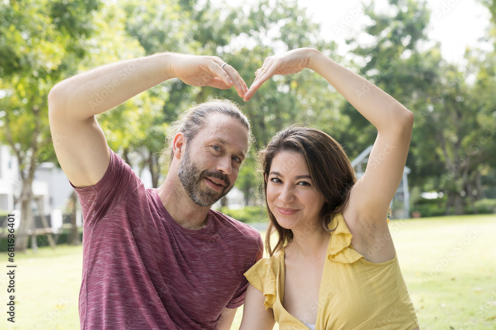 Obraz premium Happy smiling couple hugging and making heart shape outdoors in the park