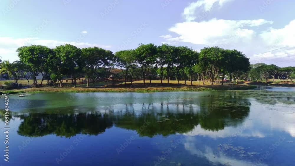 A drone hovers over a placid lake, its camera panning across the shimmering surface. The trees on the shore sway in the breeze, their leaves a brilliant green against the azure sky. A drone hovers over a placid lake, its camera panning across the shimmering surface. The trees on the shore sway in the breeze, their leaves a brilliant green against the azure sky.