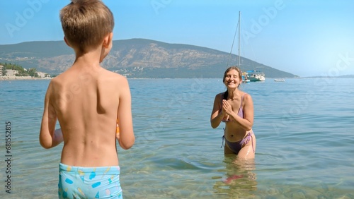 Laughing cheerful woman with her son playing frisbee and having fun on the sea beach. Family holiday, vacation and fun summertime of children and parents.